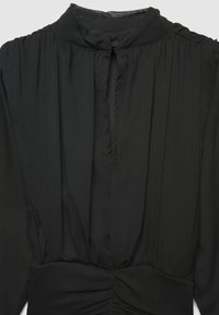 Blusa nera con colletto alto, tessuto testurizzato, pieghe verticali, chiusura con bottoni e dettagli arricciati in vita.