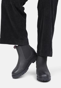 Zwarte leren enkellaarsjes met elastische zijkanten en getextureerde rubberen zolen. Gecombineerd met zwarte corduroy broeken voor een monochrome uitstraling.