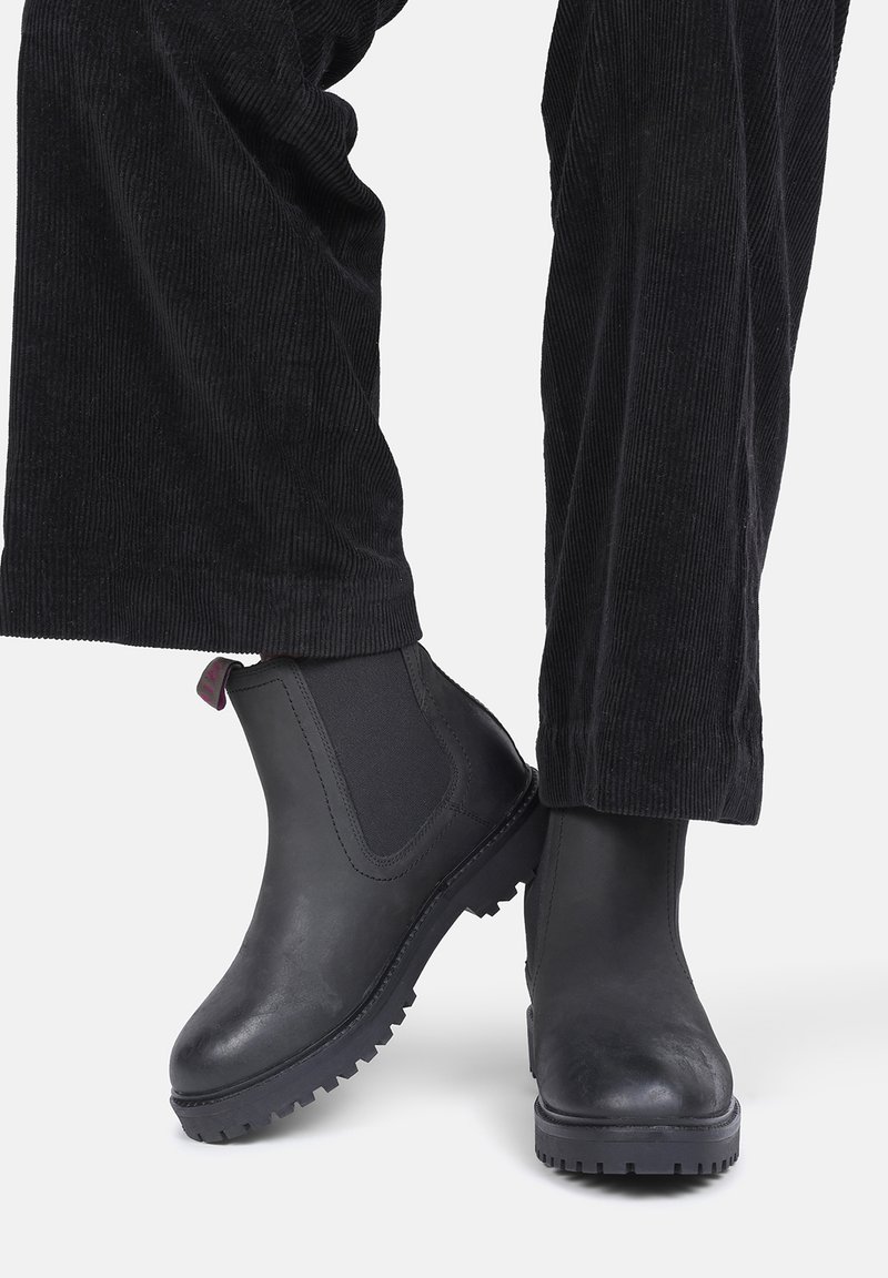 Zwarte leren enkellaarsjes met elastische zijkanten en getextureerde rubberen zolen. Gecombineerd met zwarte corduroy broeken voor een monochrome uitstraling.