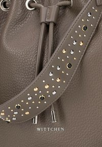 Tašky z taupe kůže se dekorativním popruhem, který obsahuje zlaté, stříbrné a černé hroty, stříbrné kovové konce na šňůrce a logo "WITTCHEN".