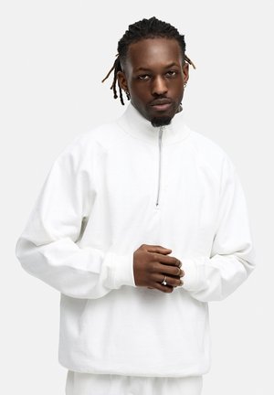 White zip-up sweatshirt with a high collar, ribbed cuffs, and a relaxed fit. Soft cotton material and minimalistic design.