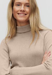 Beige, räfflad tröja med hög hals och långa ärmar. Mjuk textur, figursydd design och subtil detalj vid halsringningen.