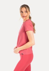 Camiseta deportiva de manga corta en vibrante color coral, fabricada con tela suave y elástica. Presenta un cuello redondo y un diseño ajustado.