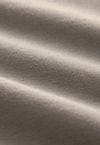Primo piano di tessuto beige strutturato con motivo a maglia fine e pieghe delicate che creano ombre morbide.