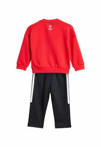 Sudadera roja con puños y cuello acanalados, combinada con pantalones de chándal negros que tienen franjas blancas en los lados, fabricados en una tela suave.