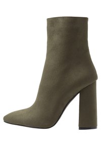 Bottine verte olive avec un talon bloc haut, fabriquée en matériau doux imitant le daim, dotée d'un bout pointu et d'une texture lisse.
