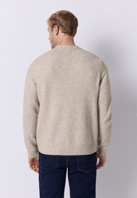 Beiger Wollpullover mit geripptem Saum, Rundhalsausschnitt und langen Ärmeln. Sanfte Textur mit entspannter Passform, kombiniert mit einer dunklen Jeans.
