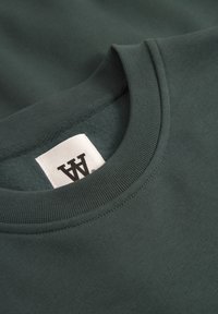 Dunkelgrüner Sweatshirt mit geripptem Rundhalsausschnitt, ausgestattet mit einer weichen Innenseite und einem angenähten Etikett am Kragen.