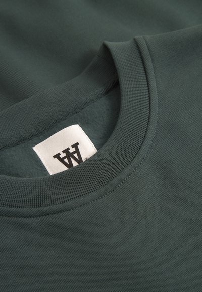 Sweatshirt vert foncé avec un col ras du cou côtelé, doté d'une texture intérieure douce et d'une étiquette cousue au col.