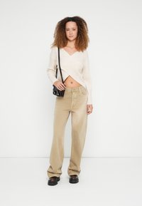 Beige cropped trui met een V-hals en een geribbelde textuur, gecombineerd met losse, hoog getailleerde beige corduroy broek en stevige zwarte plateauzolen.