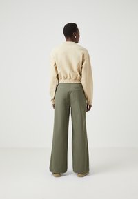 Felpa beige accorciata con orlo elastico, abbinata a pantaloni larghi verde oliva. Tessuto liscio, design minimale e senza patterns visibili.