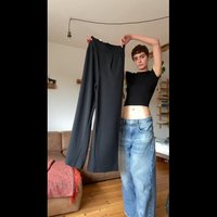 Calças pretas de cintura alta com cintura elástica com babados e bolsos laterais, exibidas com um top preto cropped contra um fundo neutro.
