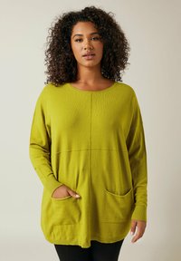 Langärmliger, lockerer grüner Pullover mit zwei Vordertaschen, gerippten Bündchen und rundem Ausschnitt. Weicher Stoff und einfarbig.