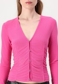 Pink long-sleeve top with a V-neck, featuring ruching on the sides and decorative silver-tone buttons down the front. Smooth fabric texture.