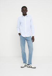 Ανοιχτό μπλε πουκάμισο με κουμπιά και διακριτικό μοτίβο, συνδυασμένο με ανοιχτό μπλε τζιν και μαυροάσπρα αθλητικά παπούτσια. Απλός σχεδιασμός και μοντέρνα εφαρμογή.