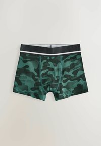 Boxers moulants verts camouflés avec une taille noire et des accents blancs. Fabriqués en tissu lisse avec des motifs graphiques et des détails textuels.