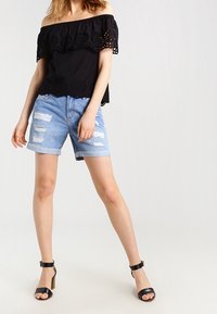 Top negro sin mangas con encaje, combinado con pantalones cortos de mezclilla azul claro desgastados y sandalias de tacón negras.