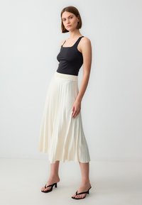 Zwarte tanktop met vierkante hals, ivoorkleurige geplooide midirok met elastische tailleband, gedragen met zwarte hoge hakken. Eenvoudig en elegant ontwerp.