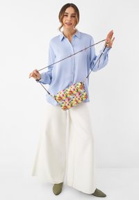 Borsa a tracolla floreale con un motivo colorato di fiori, forma rettangolare, materiale in tessuto e tracolla regolabile.