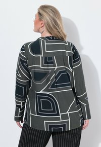 Langærmet bluse i mørkegrøn med geometriske mønstre i grå og hvid. Har en afslappet pasform og detaljer med plissé bagpå.