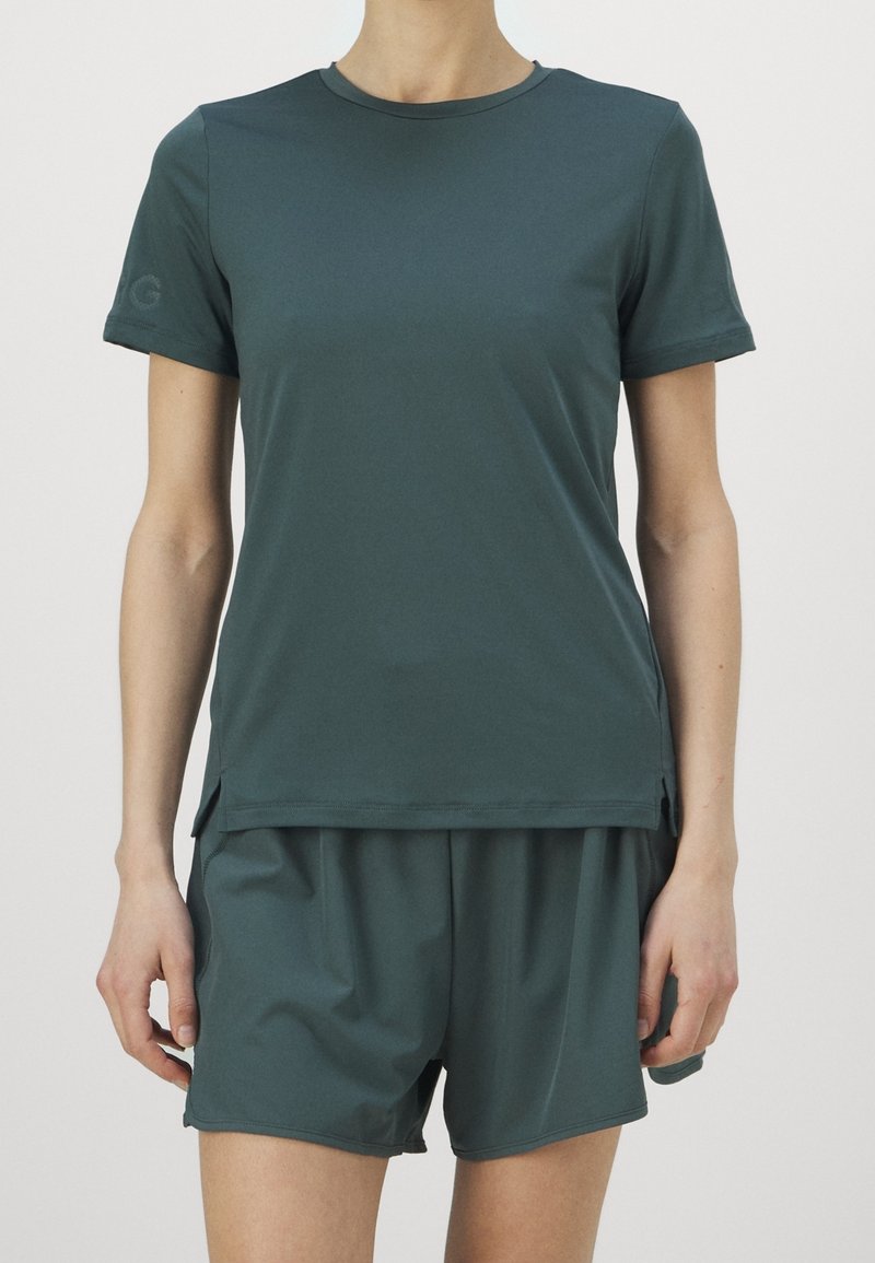 Tyrkysová sportovní souprava obsahující tričko s krátkým rukávem a volné šortky, vyrobená z lehké tkaniny se bočními rozparky pro snadný pohyb.