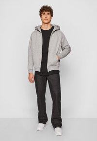 Gray zip-up hoodie with a drawstring hood, paired with a black shirt and dark denim pants, finished with white sneakers.