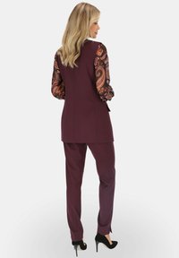 Bordowy garnitur z dopasowaną marynarką i pasującymi spodniami. Długie wzorzyste rękawy w kolorze czarnym i pomarańczowym z wzorem paisley. Czarne szpilki.