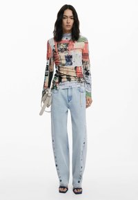 Top aderente a maniche lunghe con stampa astratta multicolore; abbinato a jeans a gamba larga di colore blu chiaro con dettagli a bottoni lungo il lato.