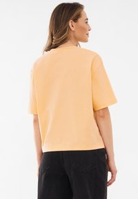 Losse, korte mouwen t-shirt in zacht, lichtoranje katoen. Ronde halslijn, minimalistisch ontwerp, gecombineerd met high-waisted zwarte denim broek.