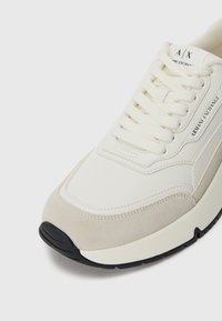 Hvite og beige Armani Exchange-sneakers med teksturert såle, snøring og merket logo på siden og tungen.