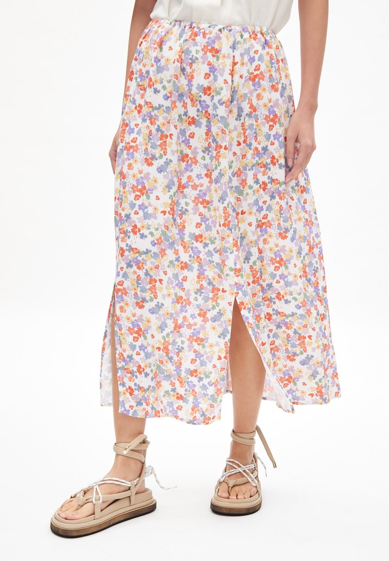 Jupe midi à imprimé floral avec de petites fleurs multicolores sur un fond clair, comportant une fente sur le côté. Associée à des sandales beiges à lanières.