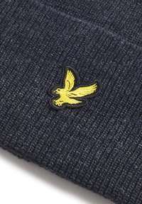 Marineblå strikket lue med ribbet tekstur som har en gul brodert fuglelogo foran, omrisset i svart.