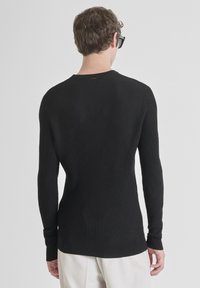 Maglione nero a costine con maniche lunghe, scollo rotondo e un motivo delicato sulla parte posteriore. Tessuto morbido e design aderente.