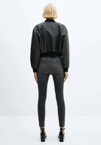 Chaqueta bomber negra recortada con puños acanalados, combinada con jeans ajustados de color gris oscuro. Los zapatos son negros con un tacón grueso y ataduras en el tobillo.