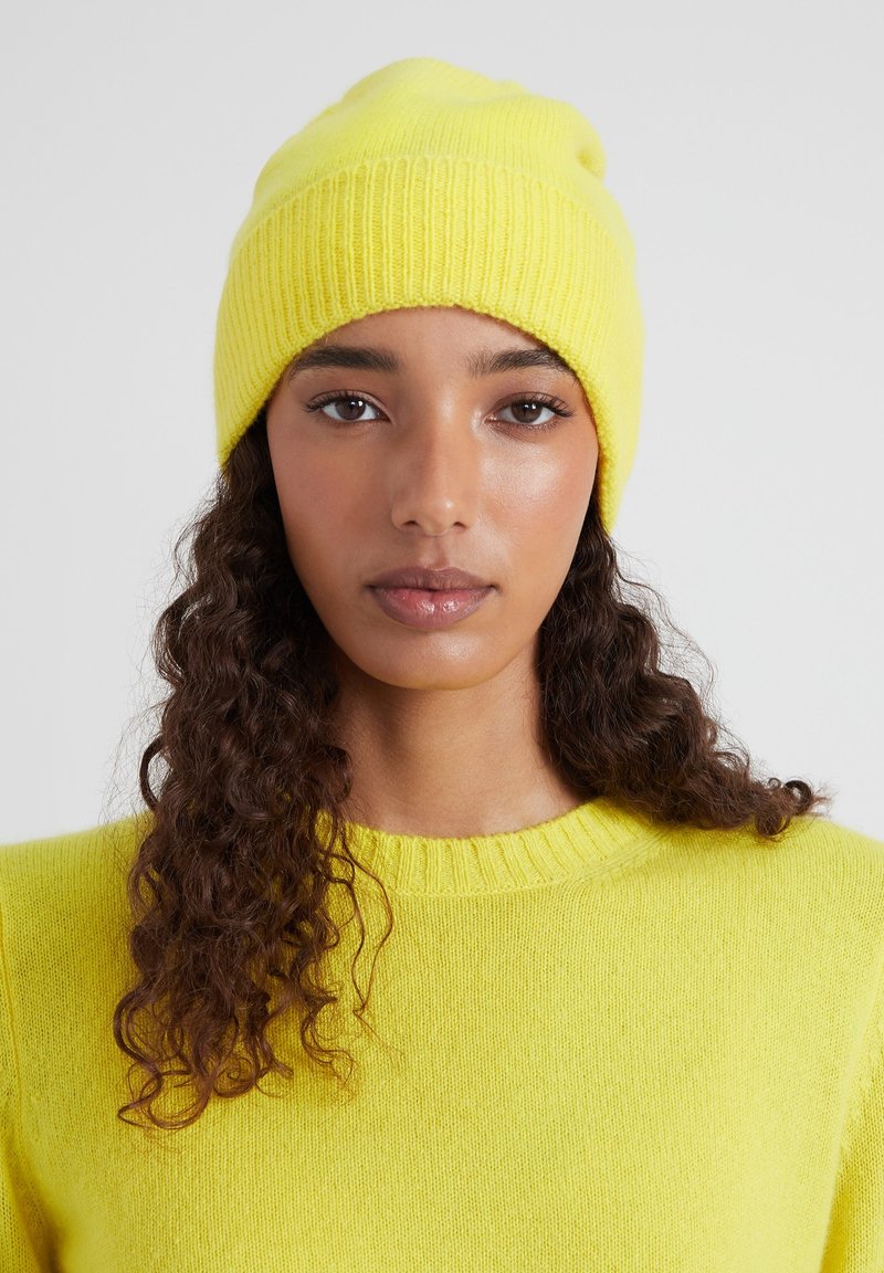 Berretto a maglia giallo brillante con texture a coste; indossato con un maglione giallo abbinato, caratterizzato da un colletto rotondo e un tessuto morbido.