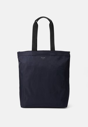 Sac fourre-tout en nylon marine avec poignées en toile noire, de forme rectangulaire, au design minimaliste, affichant un petit logo et une texture lisse.