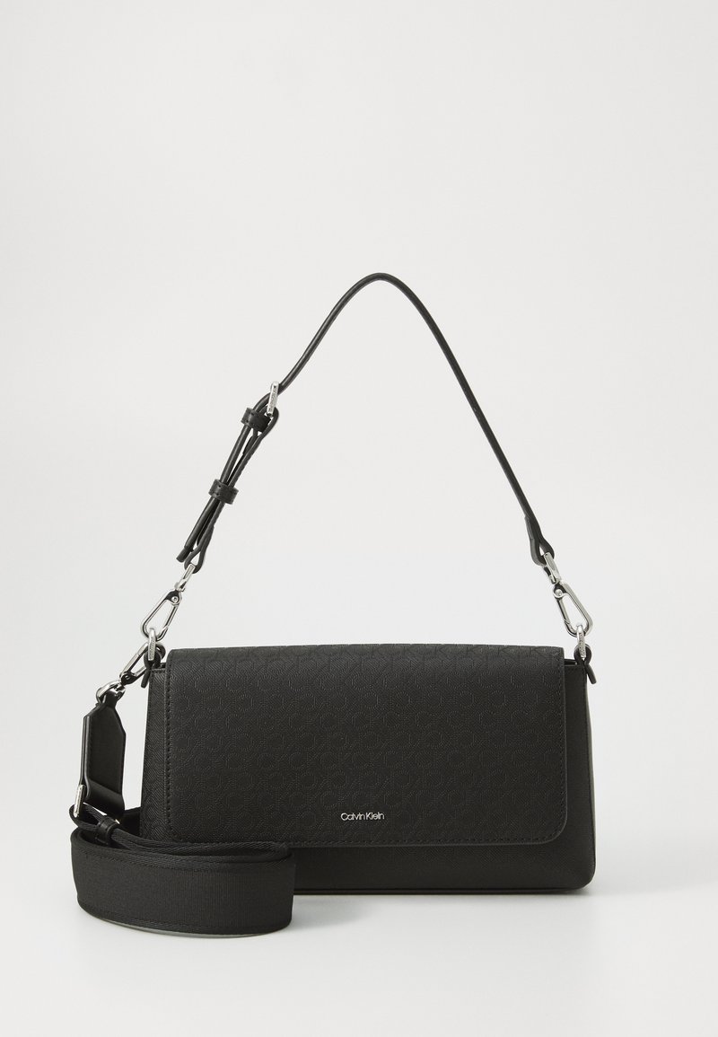 Svart crossbody-veske i teksturert materiale, med sølvfarget detaljer og justerbar stropp. Har klaffelukking og diskret merkevare.