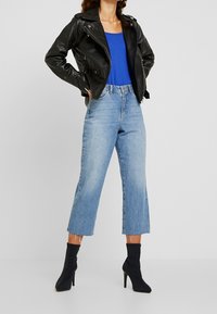 Czarna skórzana kurtka motocyklowa noszona na niebieskim topie, zestawiona z jasnoniebieskimi, szerokimi dżinsami i czarnymi botkami na wysokim obcasie.