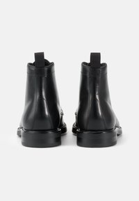 Botines negros de cuero con un acabado suave, lengüeta en la parte trasera y una suela de goma negra resistente. Detalles de costura visibles.