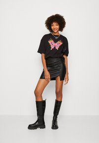 T-shirt nera con grafica di una farfalla rosa, abbinata a una mini gonna in finta pelle nera con uno spacco laterale e stivali neri al ginocchio.