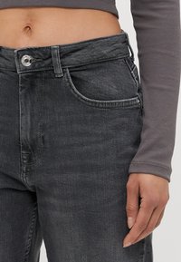 Temno sivi denim kavbojke z visokim pasom, ki imajo gumbasto zapiranje, sprednje žepe in rahlo blede teksture.