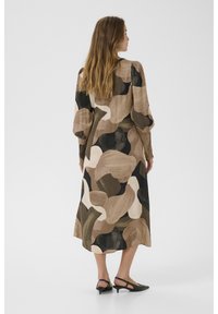 Ilga rankovė suknelė, pagaminta iš laisvai krentančios medžiagos, su abstrakčiais raštais žemės tonais: ruda, kreminė ir juoda, su atsipalaidavusiu siluetu.