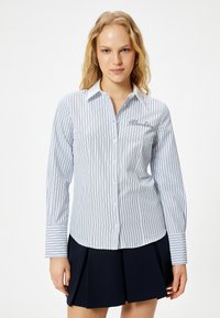 Camicia a righe blu e bianche con colletto a punta e testo ricamato. Maniche lunghe con polsini a righe contrastanti.