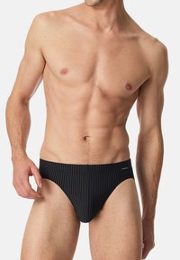 Schwarze Schwimmbrieft mit weißen vertikalen Streifen. Hergestellt aus glattem Material, mit einem niedrig geschnittenen Saum und minimalem Schnitt.
