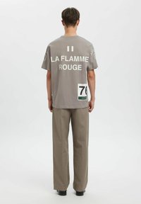 Grå bomulls-t-skjorte med hvit tekst: "II LA FLAMME ROUGE." Stor trykt nummer "70" på siden og en grønn aksenttagg. Løs passform.