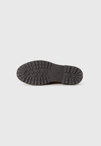 Semelle en caoutchouc noir avec des motifs de traction prononcés, y compris des crans circulaires et rectangulaires. Talon renforcé. Forme légèrement incurvée.