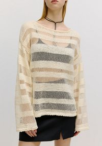 Cremefarbener Strickpullover mit offener Maschenstruktur und horizontalen Streifen in Beige und Schwarz. Weite Ärmel und ein Boot-Ausschnitt. Strukturiertes Finish.