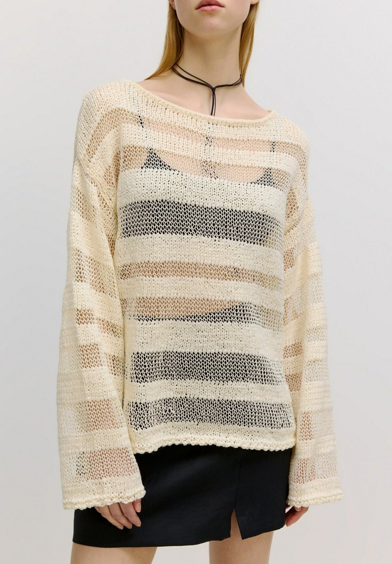 Cremefarbener Strickpullover mit offener Maschenstruktur und horizontalen Streifen in Beige und Schwarz. Weite Ärmel und ein Boot-Ausschnitt. Strukturiertes Finish.