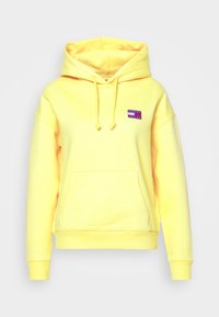 Felpa gialla in morbido tessuto, con tasca frontale, cappuccio con strings e un piccolo patch logo multicolore sul petto.
