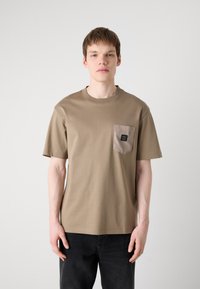 Tricou din bumbac bej cu mâneci scurte, guler rotund și o buzunar patch gri în contrast, având un logo. Croială simplă, lejeră.